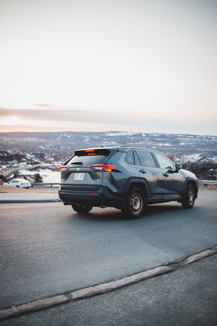 Home Contemporary black automobile riding on empty asphalt road near waterfront along calm river against hilly area and cloudy sky in coastal terrain